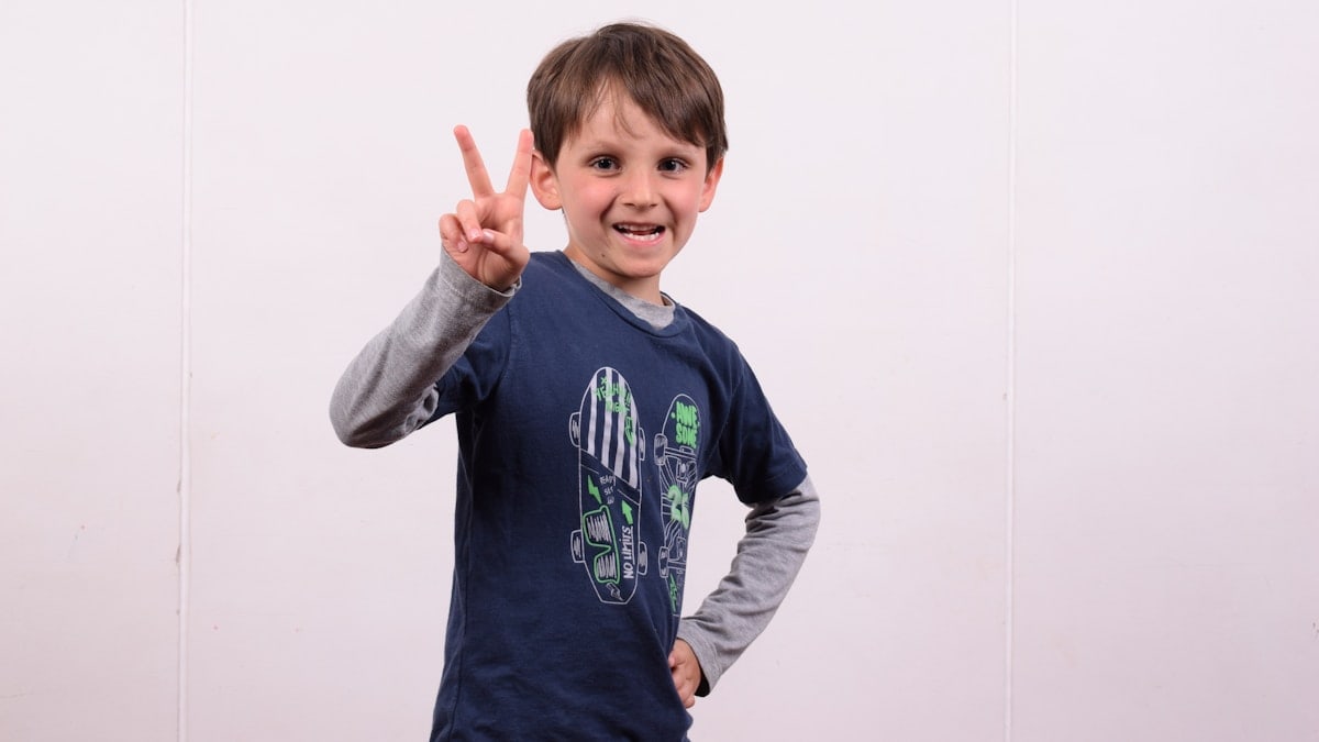 a young boy making a peace sign with his fingers